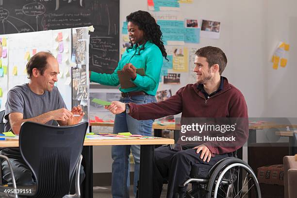Engineering Instructor Reviewing Technical Material With Students In Ideation Lab One Man With Spinal Cord Injury And Other One With Aspergers High-Res Stock Photo