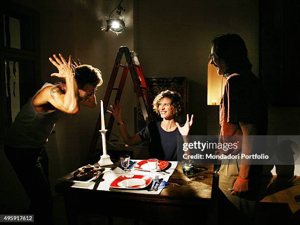 Italian actor Sergio Assisi with arms raised and Italian actress Chiara Ricci seated reciting under the eyes of the Italian director Fabrizio Costa ....