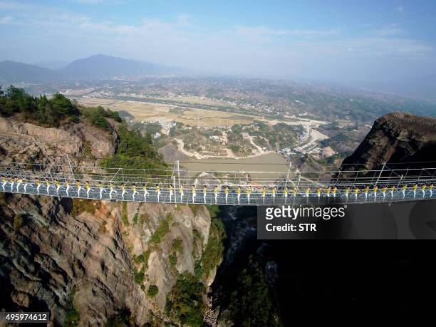 This picture taken on November 5, 2015 shows Chinese yoga fans performing on a glass-bottomed suspension bridge in the Shiniuzhai mountains in...