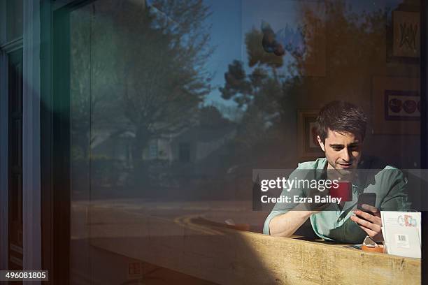 man looking at him phone in a coffee shop window - café rouge photos et images de collection