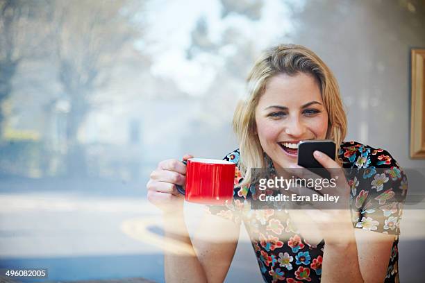 woman laughing at her phone in coffee shop window. - café rouge photos et images de collection