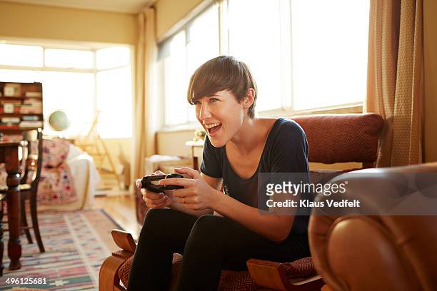 young woman playing on gaming console at home - game console stockfoto's en -beelden