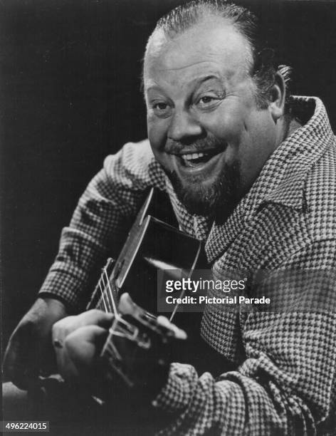 Posed portrait of actor Burl Ives playing a guitar, to promote his appearance at the Plaza Hotel, January 1950.