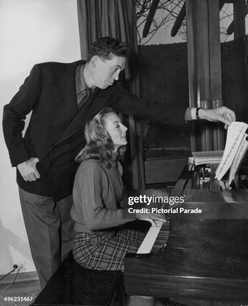 Director John Huston turning the pages of sheet music for his wife, actress Evelyn Keyes, as she plays the piano, 1948.