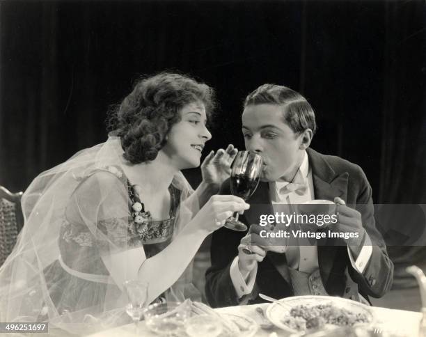 American actress Ethel Grandin holds a wine glass for a man in a tuxedo in a still from an unidentified silent film, circa 1920.