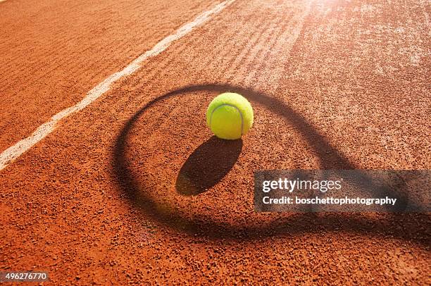 pelota de tenis y raqueta en arcilla court sombra - tennis fotografías e imágenes de stock