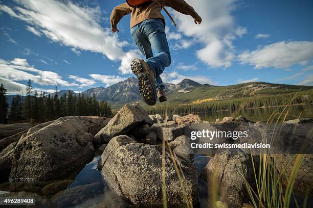hiker jumps rock to rock in mountain lake. low angle - male feet soles 個照片及圖片檔