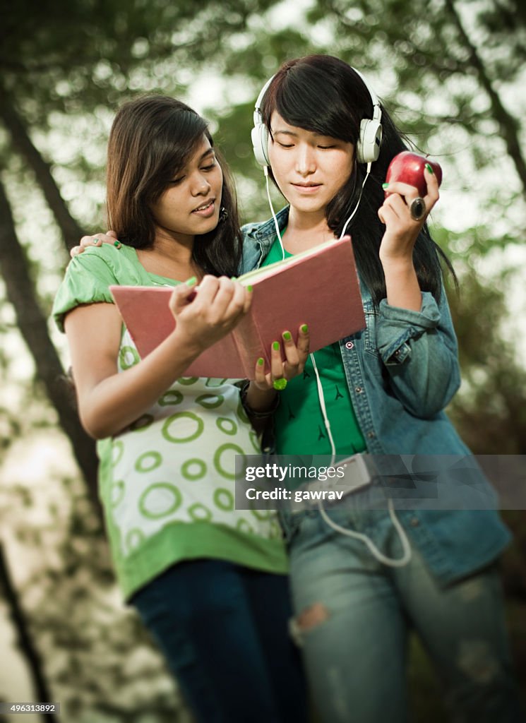 Two happy girls from different ethnicity studying together in nature.