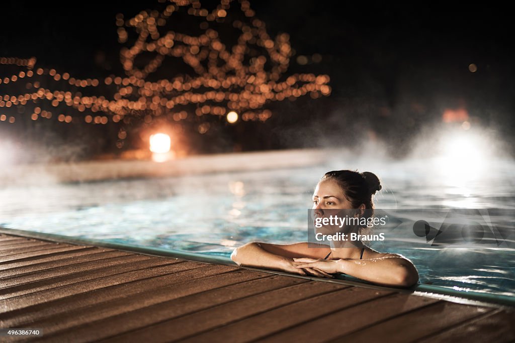 Young woman relaxing in heated swimming pool during winter night.