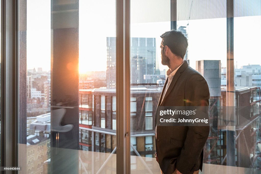 Businessman looking through office window in sunlight