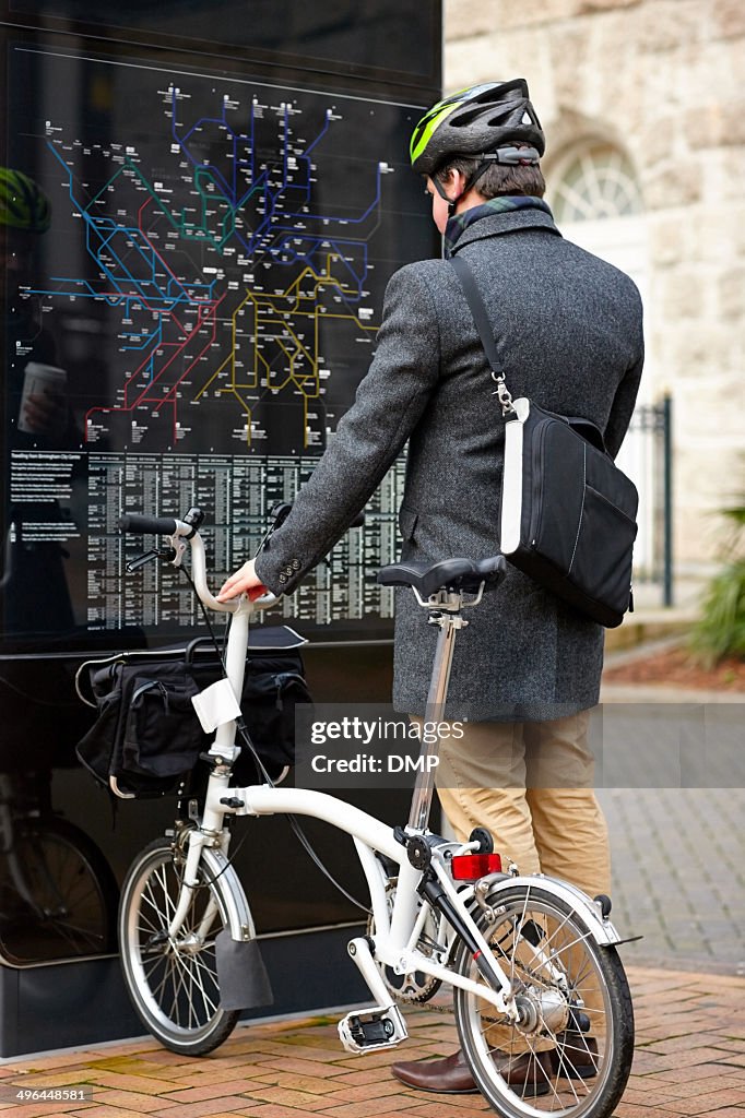 Businessman with bicycle looking at map by the city street
