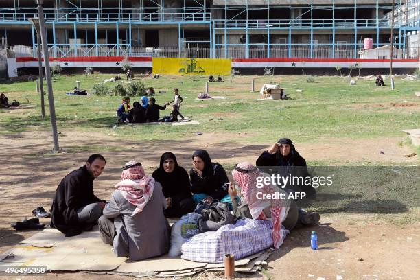 Syrians sit in a park in the capital Damascus, on November 10, 2015. Plastered on the wall in the background are a large version of the Syrian flag...