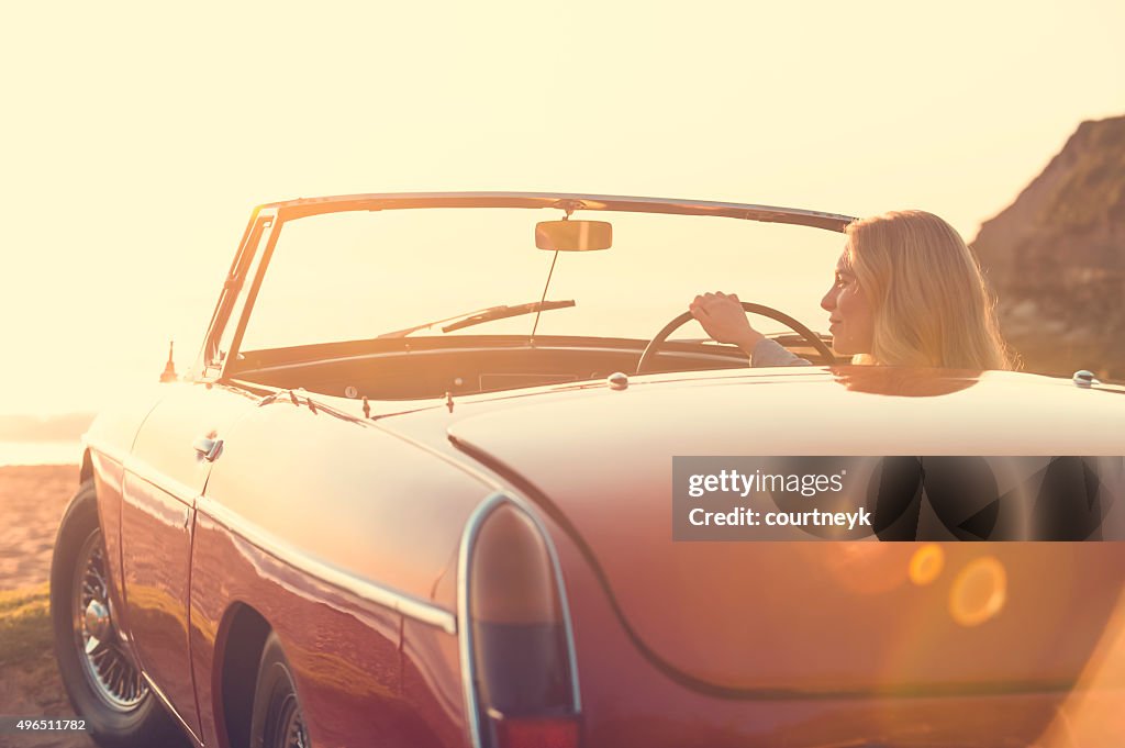 Woman driving a convertible car at the beach.