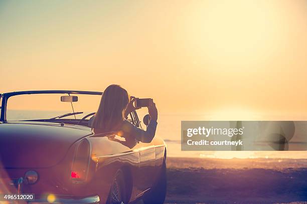 woman taking a sunset photo in a convertible car. - road trip new south wales stock pictures, royalty-free photos & images