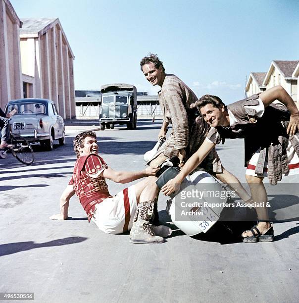 American actor Charlton Heston and British actor Stephen Boyd, wearing stage costumes, having fun in riding a Vespa and a bicycle on the set of the...
