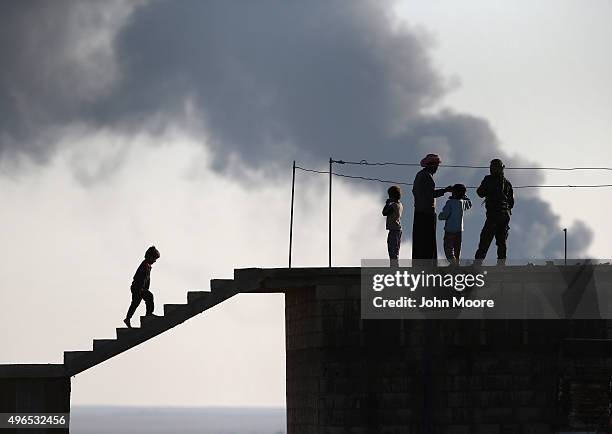 Local residents speak with a Kurdish soldier while an oil well burns in the distance on November 10, 2015 near the ISIL-held town of Hole in the...