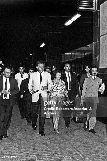 British actors Richard Burton and his wife Elizabeth Taylor arriving in Rome and walking out Termini railway station among people surrounded by...