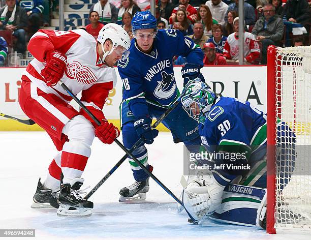Jake Virtanen of the Vancouver Canucks checks Joakim Andersson of the Detroit Red Wings as Ryan Miller of the Vancouver Canucks makes a save during...