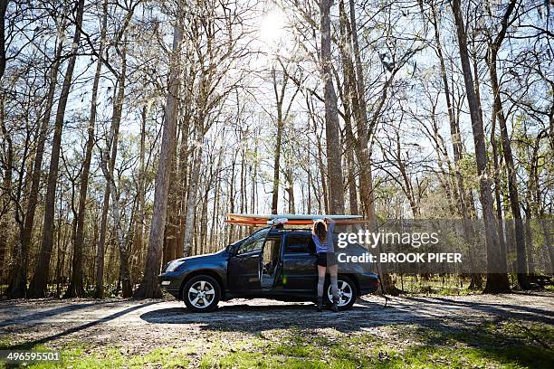 young woman strapping paddleboard to roof of car - cool cars stockfoto's en -beelden