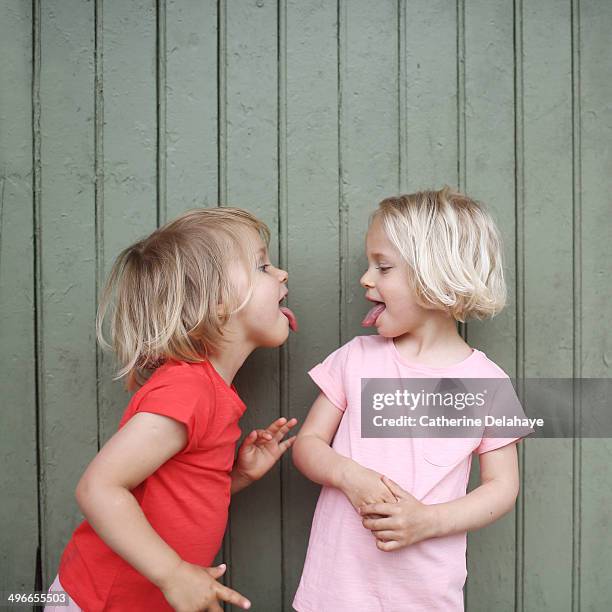 two 3 years old twins girls playing together - blonde girl sticking out her tongue stock pictures, royalty-free photos & images