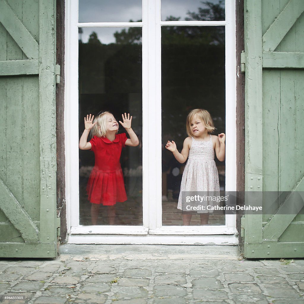 Two 3 years old twins girls posing behind a window