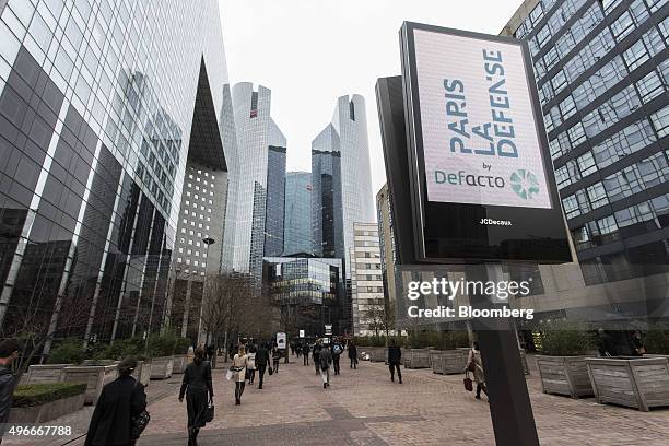 The logo of advertising company JCDecaux SA sits on an electronic screen as the headquarters of Societe Generale SA, center, stand beyond in La...