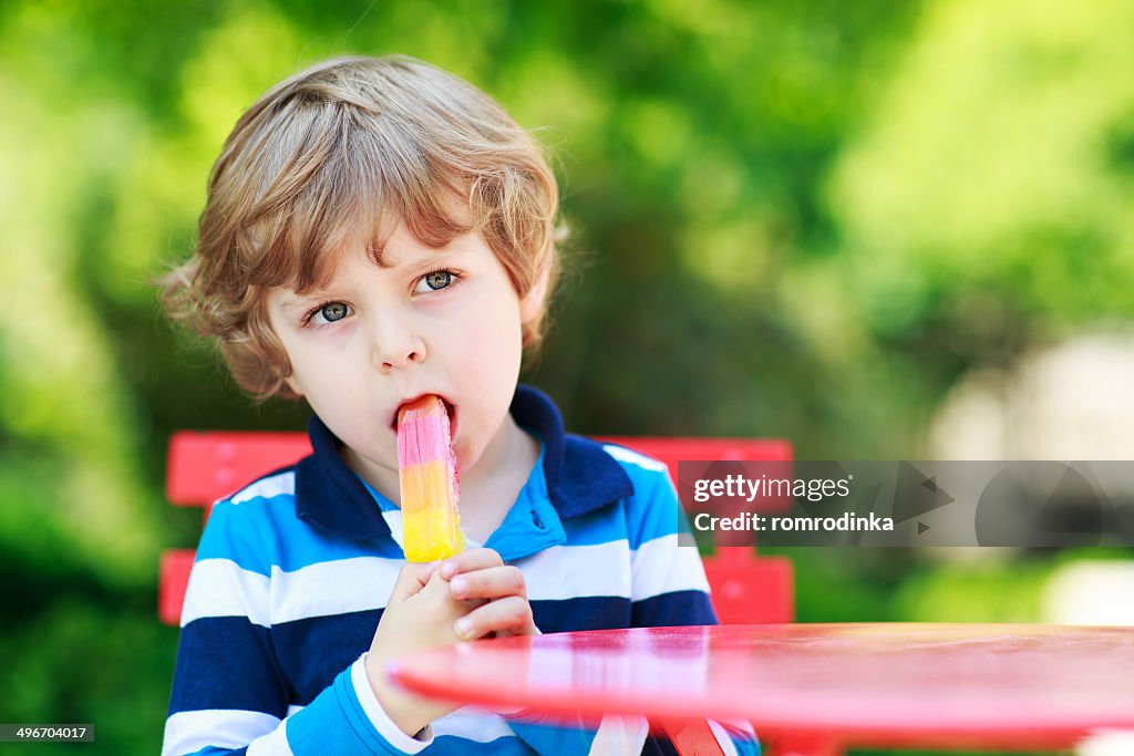 Happy little preschool boy eating colorful ice cream in summer