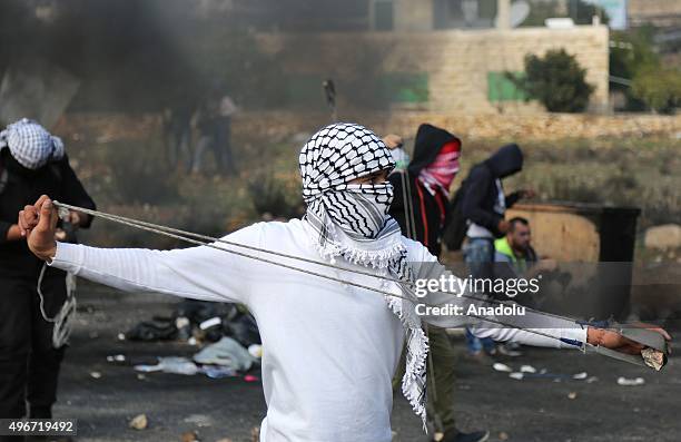 Masked Palestinian protestors who protests Israeli government's violations on Jerusalem and West Bank, uses a slingshot to hurl stone at Israeli...