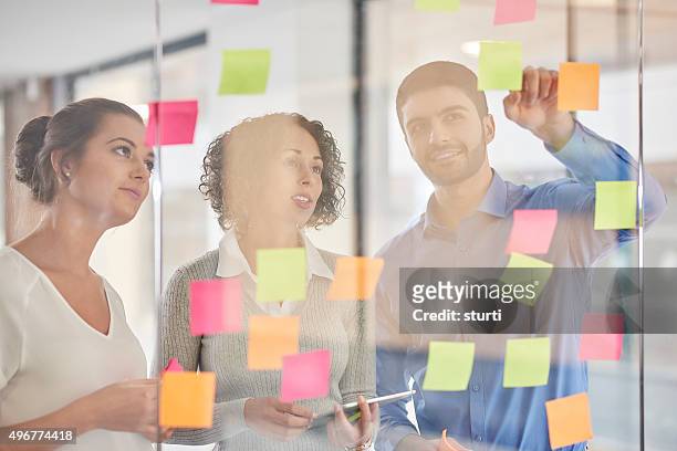 unternehmen-team-brainstorming - team looking at adhesive notes in board room during meeting stock-fotos und bilder