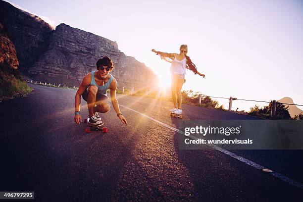 friends longboard skating on road sunset - couple skating stock pictures, royalty-free photos & images