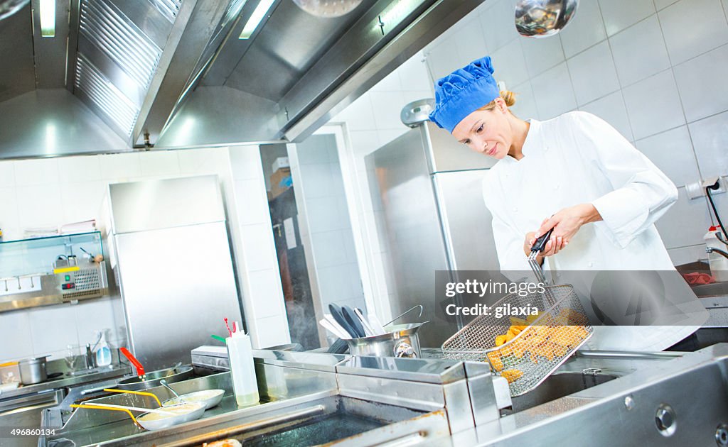 Female chef frying potatoes in restaurant kitchen.