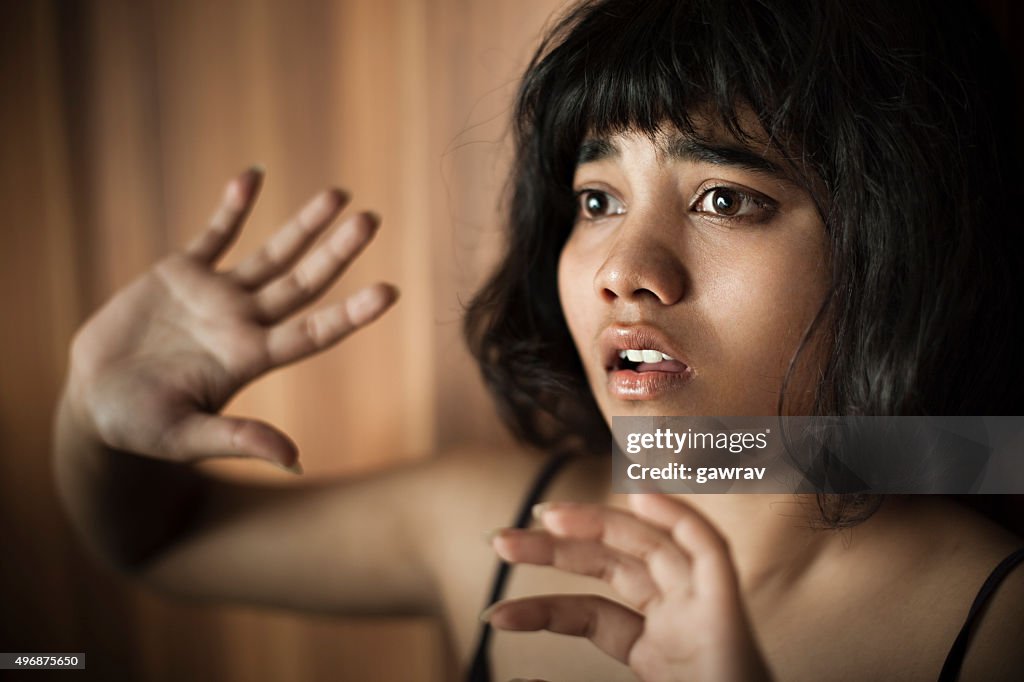 Frightened teenage girl looking away and hiding herself behind hands.