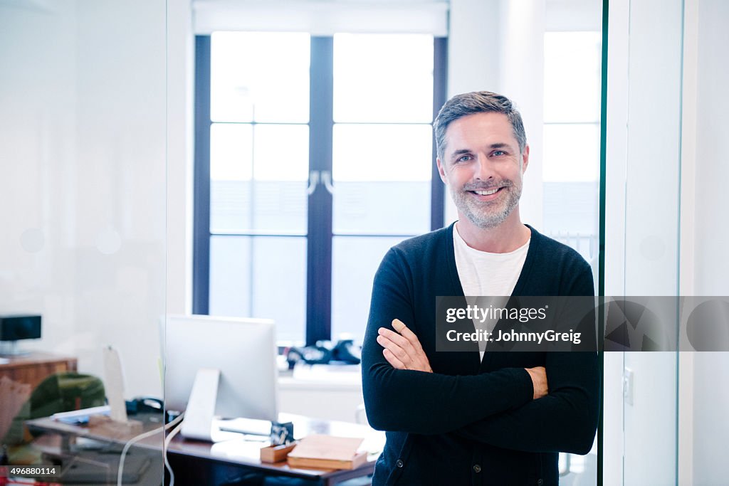 Attractive casual businessman in modern office, arms folded