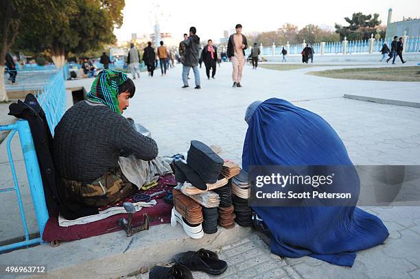 Woman wearing a blue burqa makes a purchase from a shoe repairman as Afghans go about daily life despite security fears of a resurgent Taliban across...