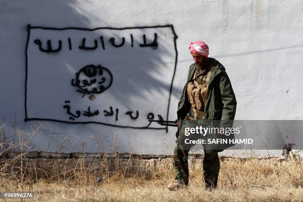 Kurdish fighter walks by a wall bearing a drawing of the flag of the Islamic State group in the northern Iraqi town of Sinjar, in the Nineveh...