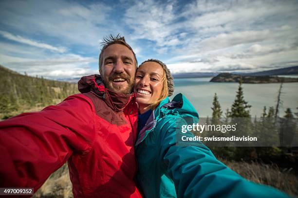 young couple hiking reaches view point and takes selfie portrait - yukon stock pictures, royalty-free photos & images