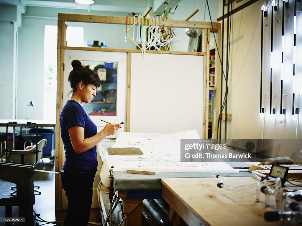 Female neon artist working on smart phone in loft