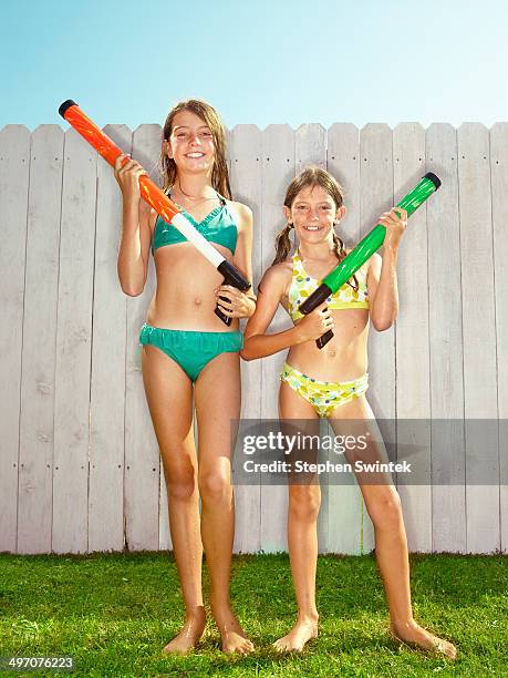 2 wet sisters pose with water toys - tween girl swimsuit stock-fotos und bilder
