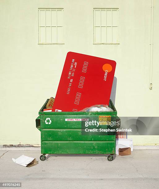 oversized credit card stuffed in dumpster - müllcontainer stock-fotos und bilder