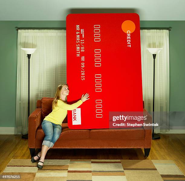 young woman snuggling with oversized credit card - credit card debt stock-fotos und bilder