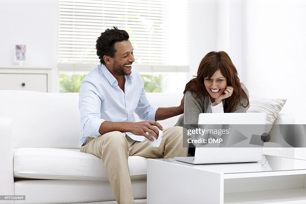Cheerful mature couple using laptop at home