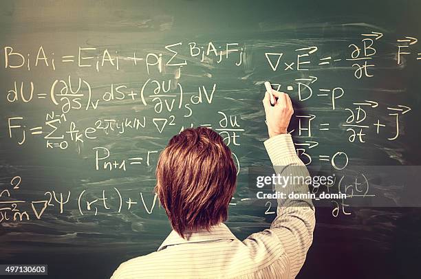 man standing against chalkboard, solves physics equations, rear view, retro - natuurkunde stockfoto's en -beelden