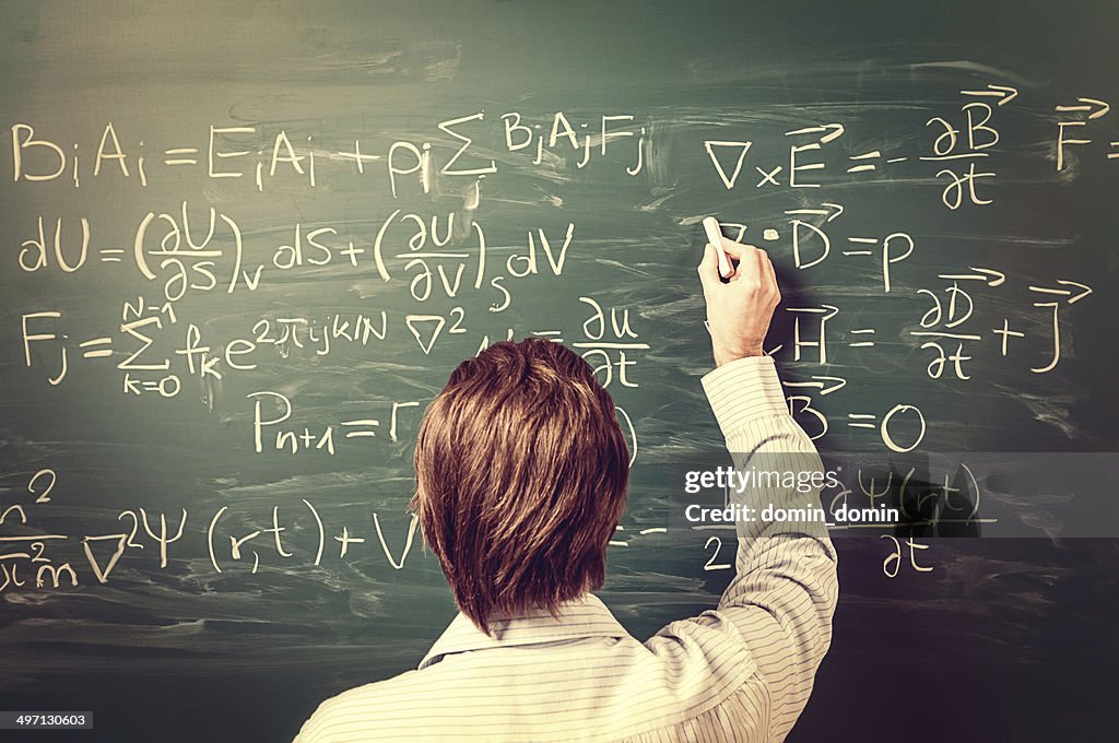 Man standing against chalkboard, solves physics equations, rear view, retro