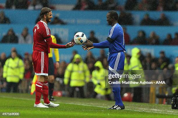 David Beckham of Great Britain and Ireland XI hands the ball to Dwight Yorke of Rest of the World XI during the David Beckham Match for Children in...