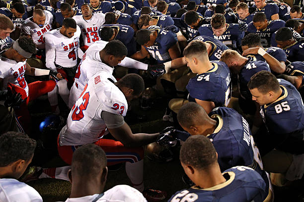 Tight end Jeremiah Gaines of the Southern Methodist Mustangs, linebacker Tyler Goble of the Navy Midshipmen and other players join hands in prayer...