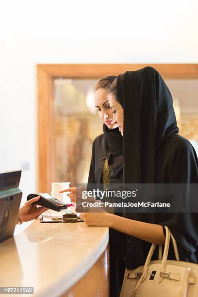 traditionally dressed emirati woman paying by credit card at counter - arab shopping stockfoto's en -beelden