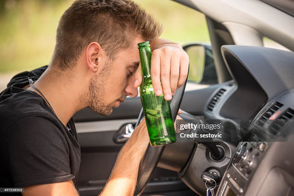 Mann trinkt Bier, während Sie ein Auto