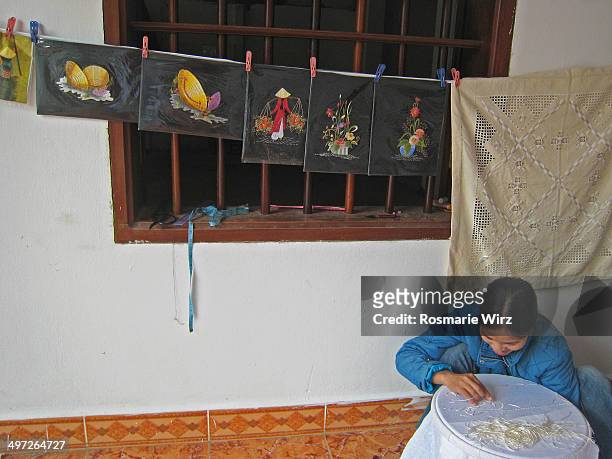 Girl sits on floor embroidering tablecloth for sale.