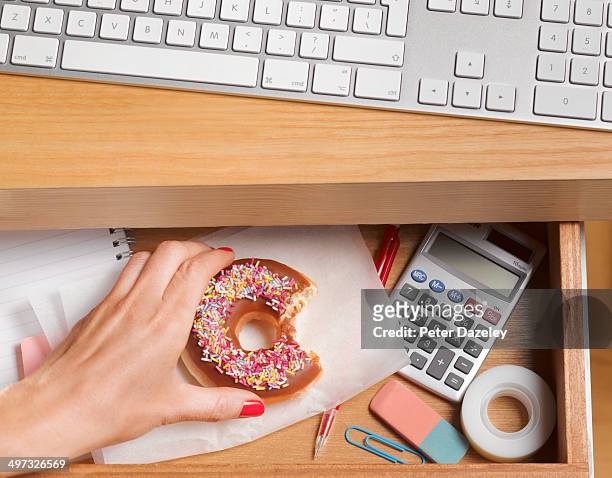 binge eater hiding doughnut in desk drawer - hambre fotografías e imágenes de stock