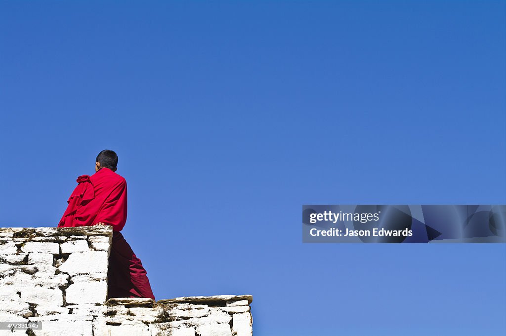 A teenage Buddhist monk sitting in the sunshine on an ancient monastery wall.